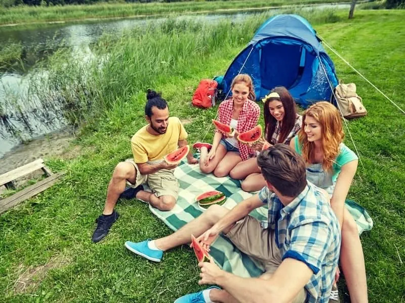 Friends camping together and sharing a meal of watermelon