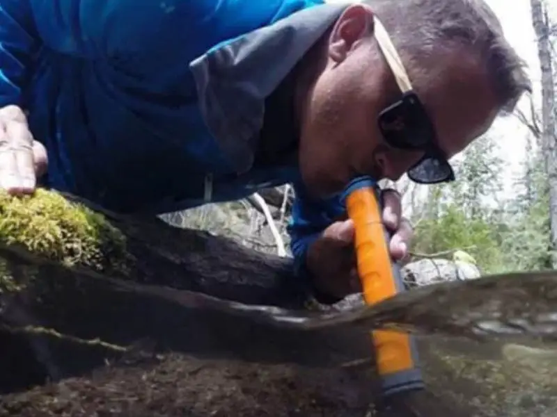 Man drinking water through a purifying water straw to make it safe