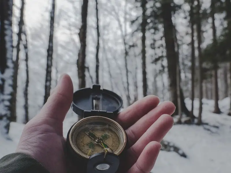 Person using compass in the woods in the winter