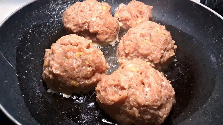 raw meatballs being cooked in a skillet