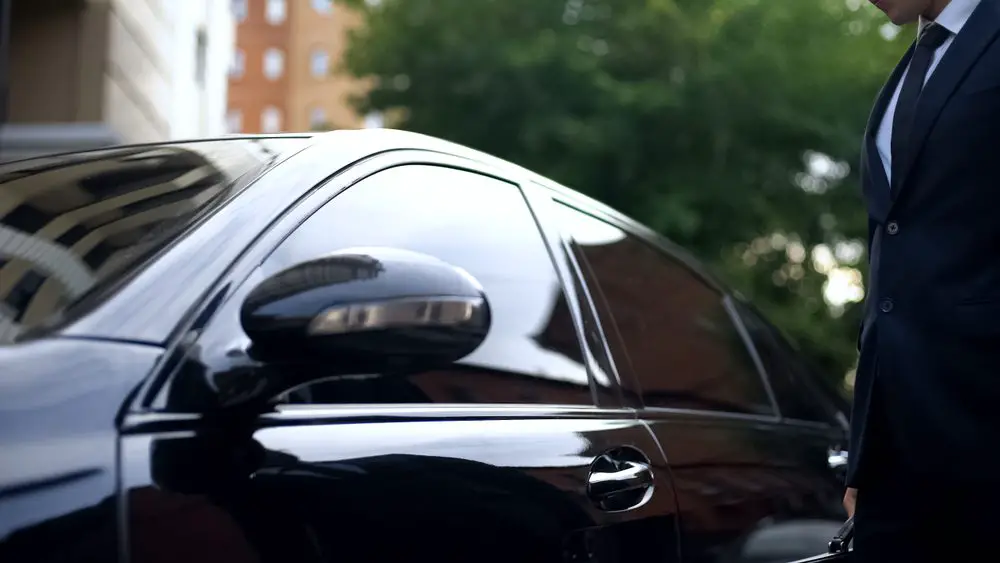 Man Wearing A Suit Standing Near A Bulletproof Car