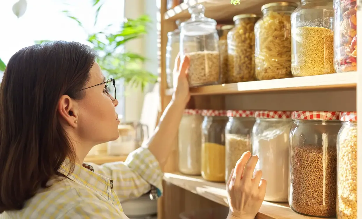 Woman stores jars with beans on shelf with other stored food